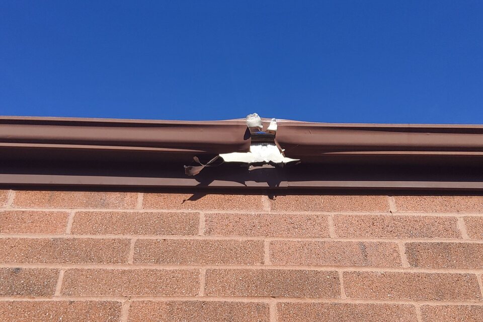 Brown metal gutter with a torn, separated seam along the top of a brick wall