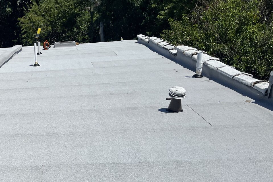 Light gray granulated modified-bitumen cap sheet on a flat roof with flashed vent pipes along a parapet wall